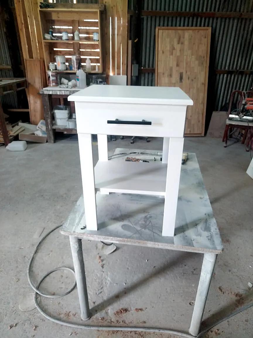 White bedside table with one drawer, a black bar handle, a lower shelf and straight legs