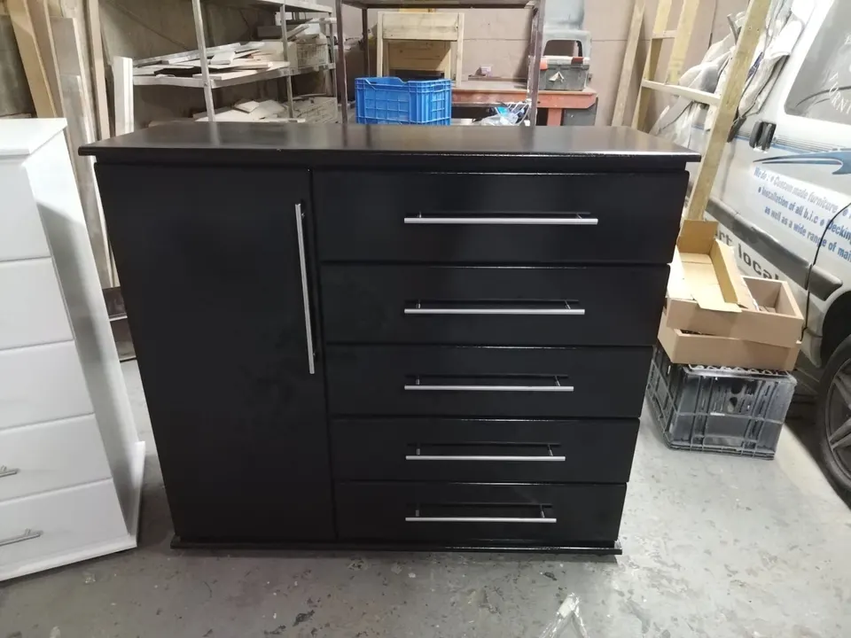 Black chest of drawers with five drawers and a tall single cupboard door on the left, with long bar handles