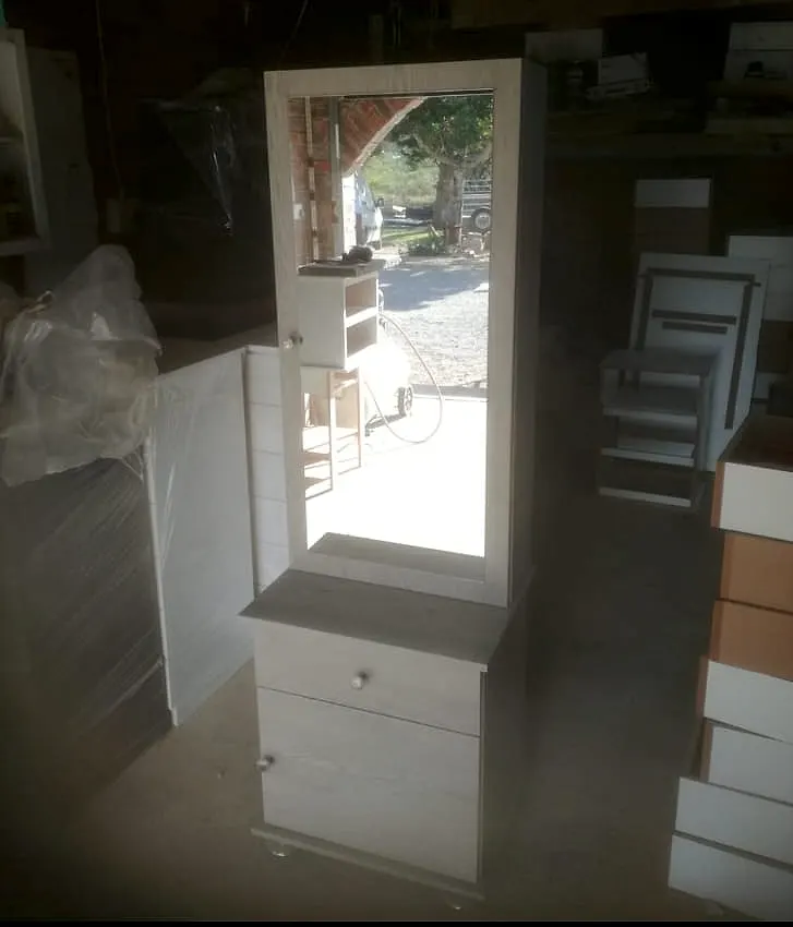 Whitewashed wooden dressing table with a tall framed mirror above a small cabinet with a drawer and a door