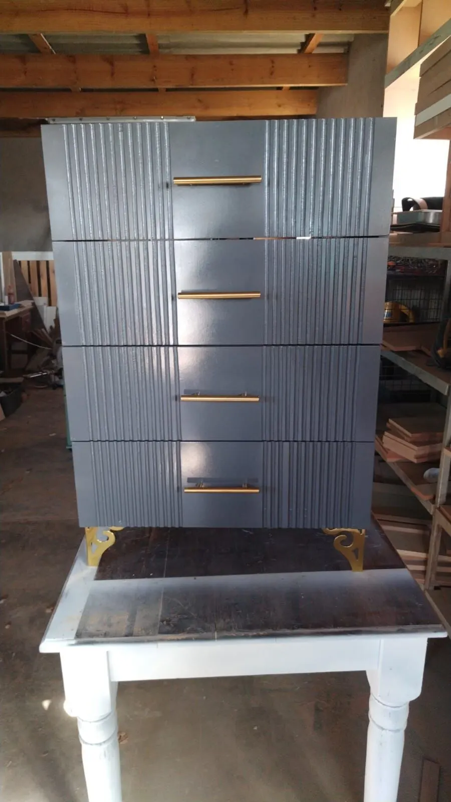 Grey four-drawer chest of drawers with vertical fluted drawer fronts, brass bar handles and gold corner feet